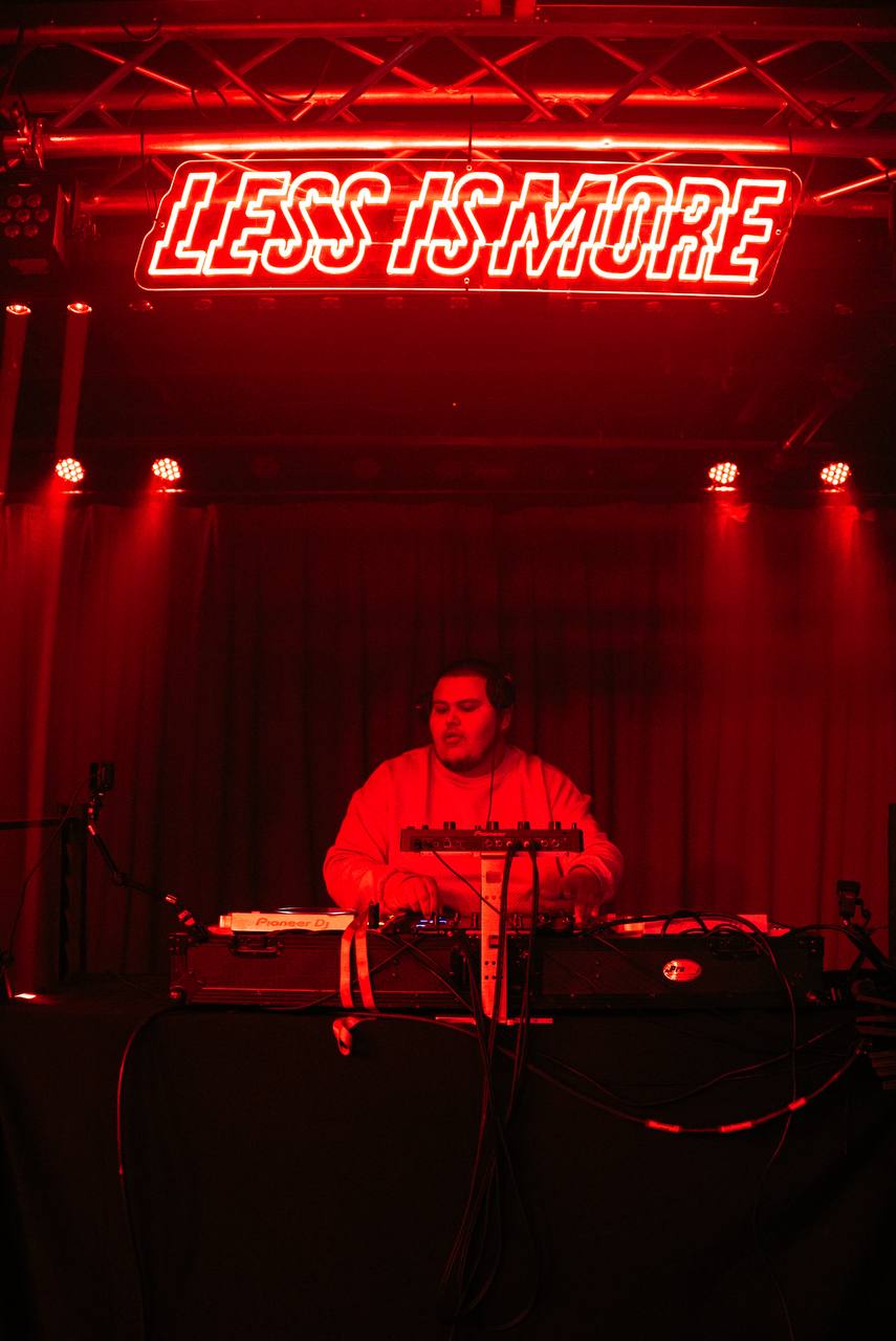 DJ under Less Is More neon sign — full stage